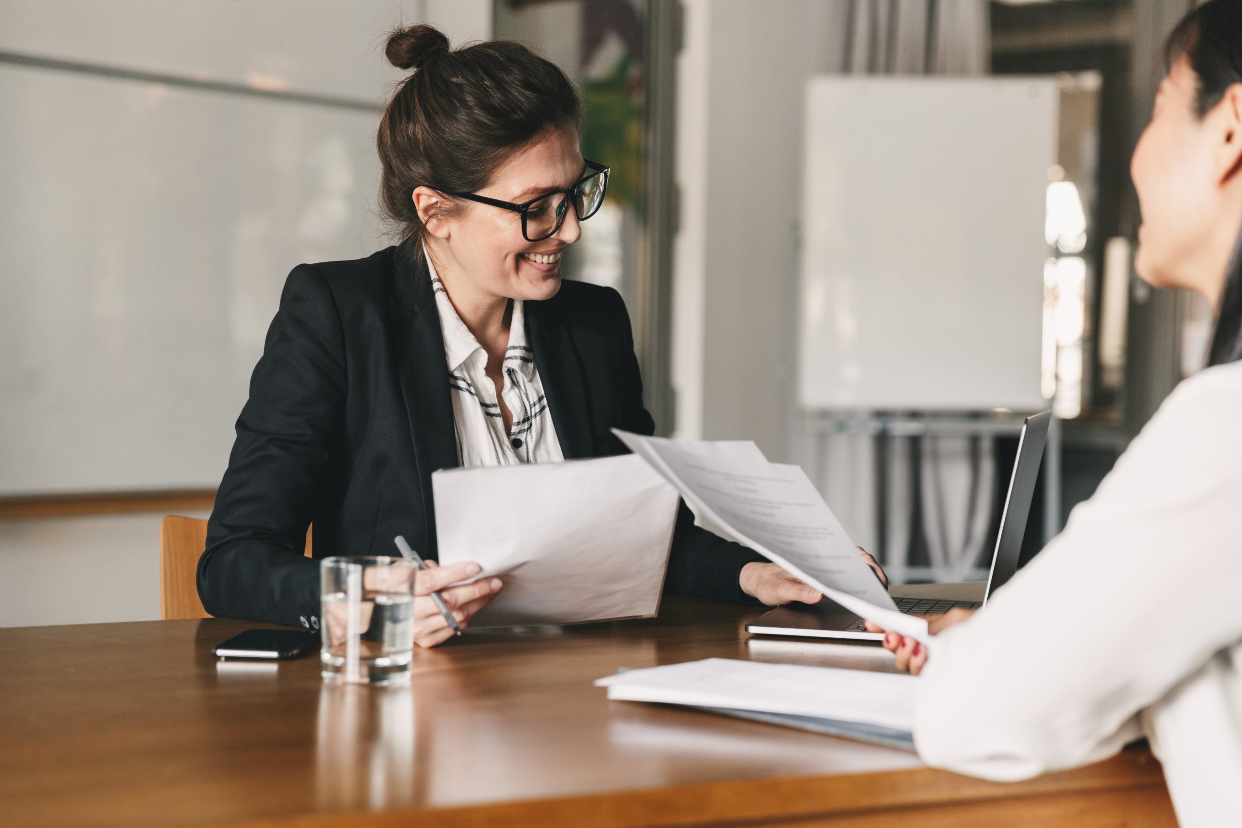 Photo of successful woman holding resume and negotiating with female candidate during corporate meeting or job interview – business, career and placement concept