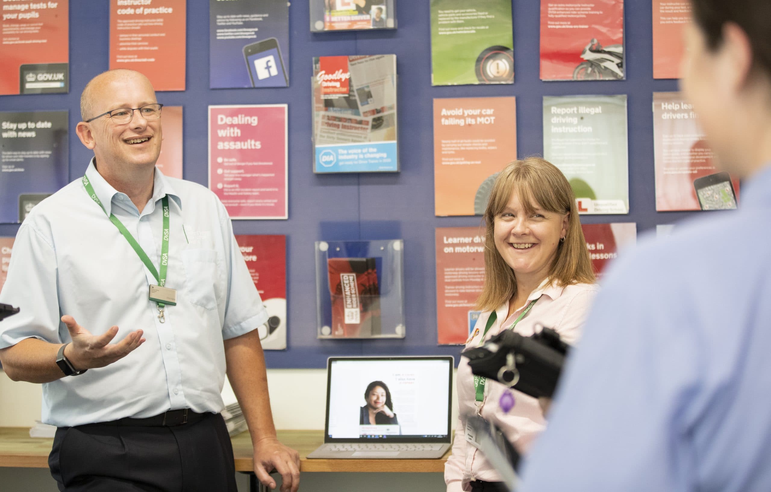 DfT staff members standing in front of the DVSA office poster-wall.