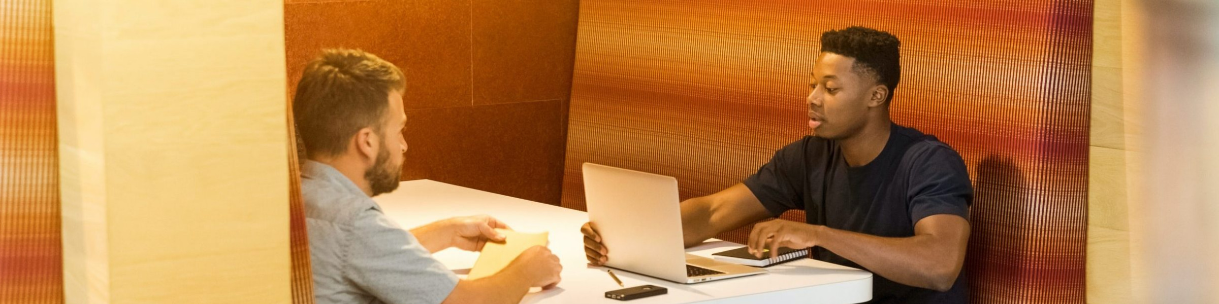 Two men sitting at a table using their laptops.